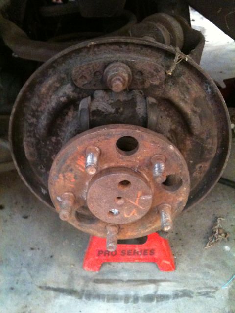 1975 Ford Ranchero - Close-up of a rusty brake drum and hub assembly supported by jack stands.