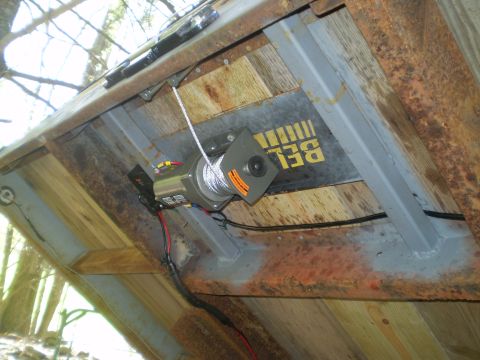 1979 Ford Bronco - A winch is mounted to a surface with visible wood and rusted metal, yellow text on a metal plate.