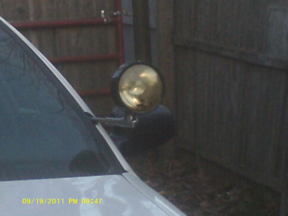 Close-up of a spotlight attached to the driver's side A-pillar of a white vehicle