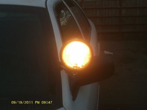 2006 Ford Crown Victoria - A close-up of a white vehicle's side mirror shows an illuminated amber turn signal light.