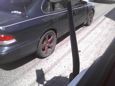 2003 Ford Crown Victoria - Side view of a dark sedan with custom wheels and visible rust on the lower body panels.