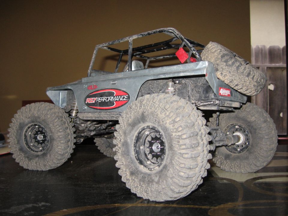 RC rock crawler with large tires, roll cage, and spare tire mounted on rear. Red and black 'PRO-PERFORMANCE' decal on side