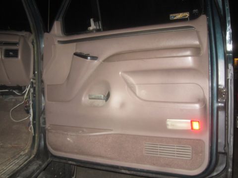 1993 Ford Bronco - The interior door panel of a vehicle is shown, a pull handle and a red illuminated light.