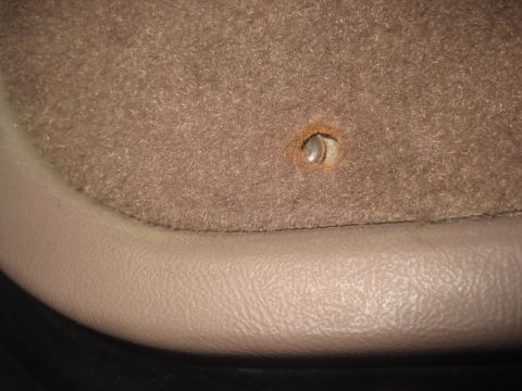 1993 Ford Bronco - Close-up of a tan carpeted interior panel with a screw hole, showing beige trim along the bottom edge.