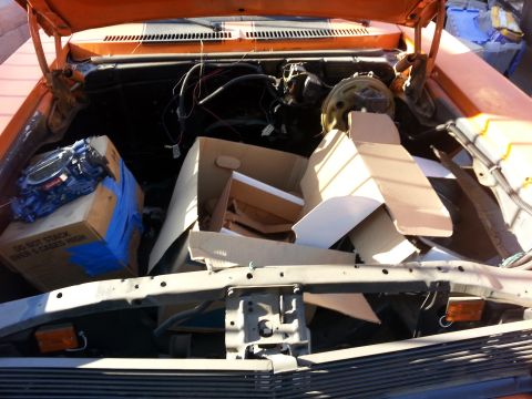 1973 Chevrolet Nova - The engine bay of an orange 1973 Chevrolet Nova is packed with boxes and parts, obscuring the engine itself.