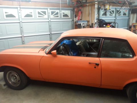 1973 Chevrolet Nova - This orange 1973 Chevrolet Nova coupe features black racing stripes and appears to be undergoing some work in a garage.