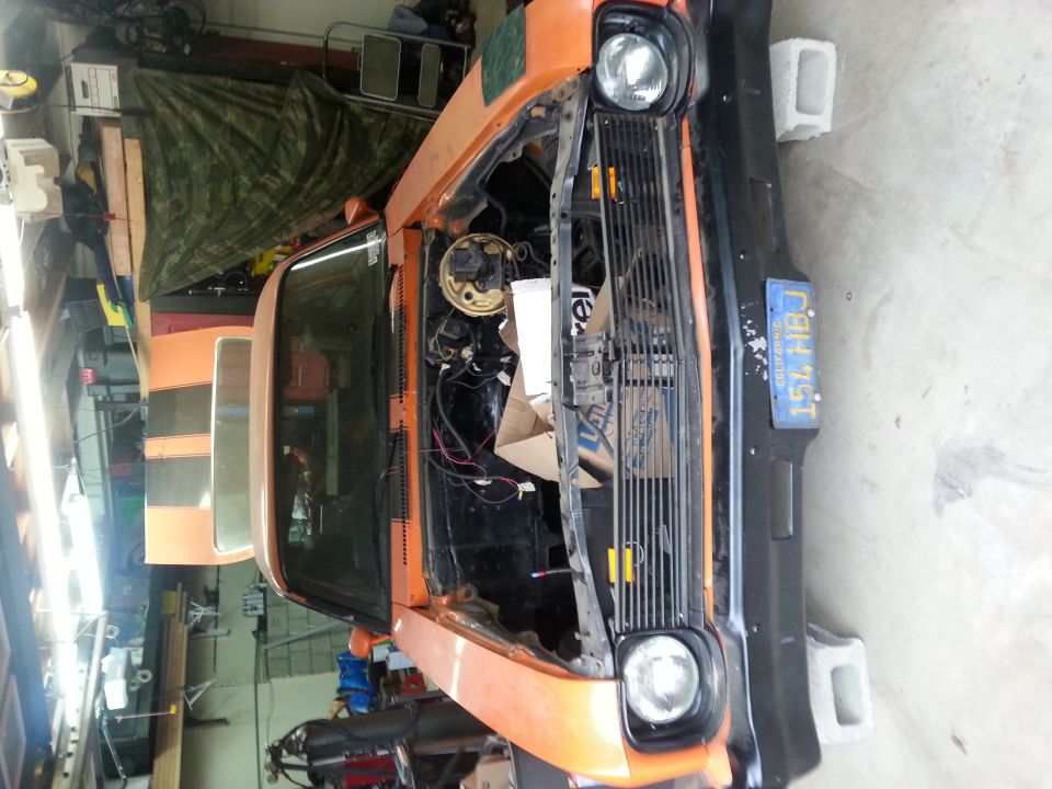 Front view of an orange car with hood open, sitting in a garage. License plate reads 154 HBJ