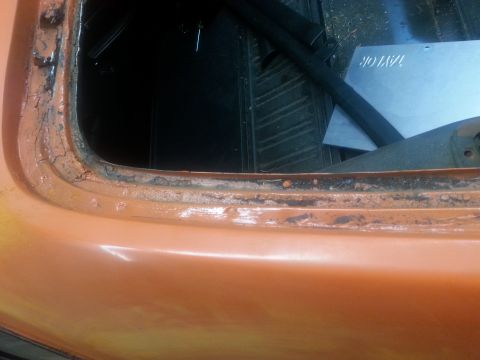 1973 Chevrolet Nova - Close-up of a corroded window seal on an orange vehicle, showing interior details.