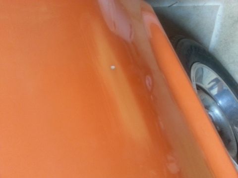 1973 Chevrolet Nova - Close-up of an orange car's body panel, revealing a minor imperfection and a wheel.