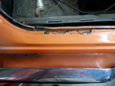 1973 Chevrolet Nova - Close-up of rust damage on a car's door sill, with a chrome trim piece visible below.