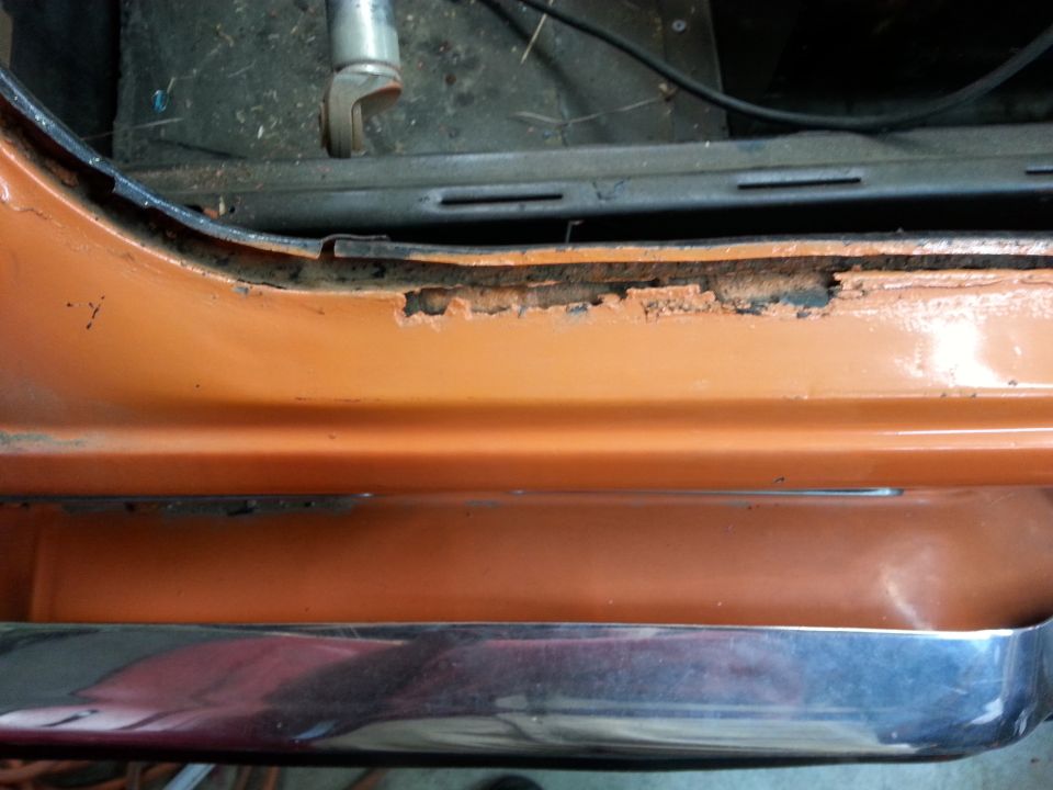 rusted door sill and chrome trim on an orange car