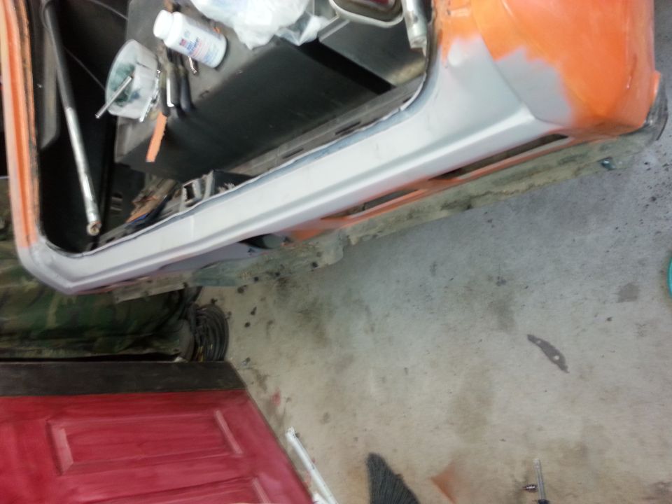 Orange car door interior with gray primer on the rocker panel, tools and bottles on the seat