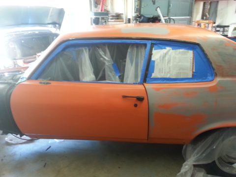 1973 Chevrolet Nova - Car body in primer and orange paint, taped off for prep work. Another car is visible in the background.