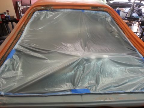 1973 Chevrolet Nova - The interior of an orange car is covered in plastic sheeting and blue tape, preparing for paint work.