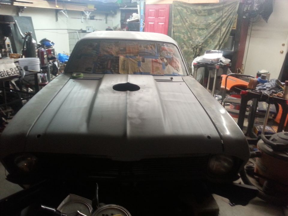 1973 Chevrolet Nova front end, hood has a hole cut in it, car is in a garage