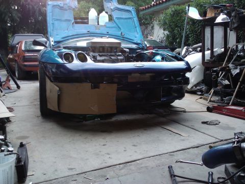 1995 Ford Probe - A 1995 Ford Probe is undergoing repairs in a garage, its hood and engine exposed.