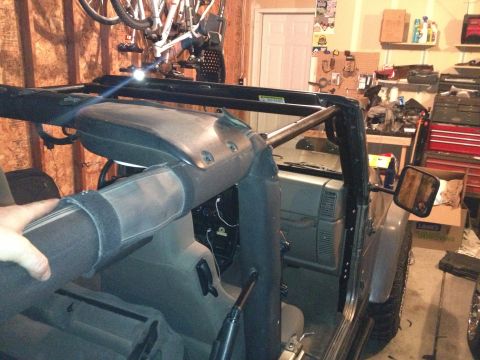 2005 Jeep Wrangler - The interior of a Jeep is shown with a roll cage and a hand adjusting the soft top.
