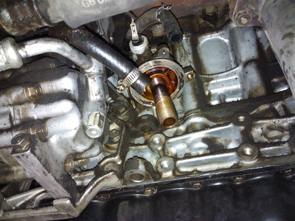 Engine oil filter housing with hoses attached, showing metal and oil residue
