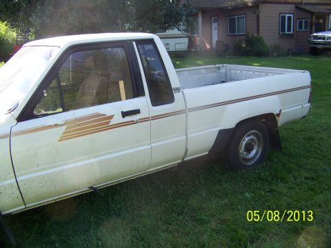 1988 Suzuki Samurai - Side view of a white pickup truck with a gold stripe decal on the door and bed.