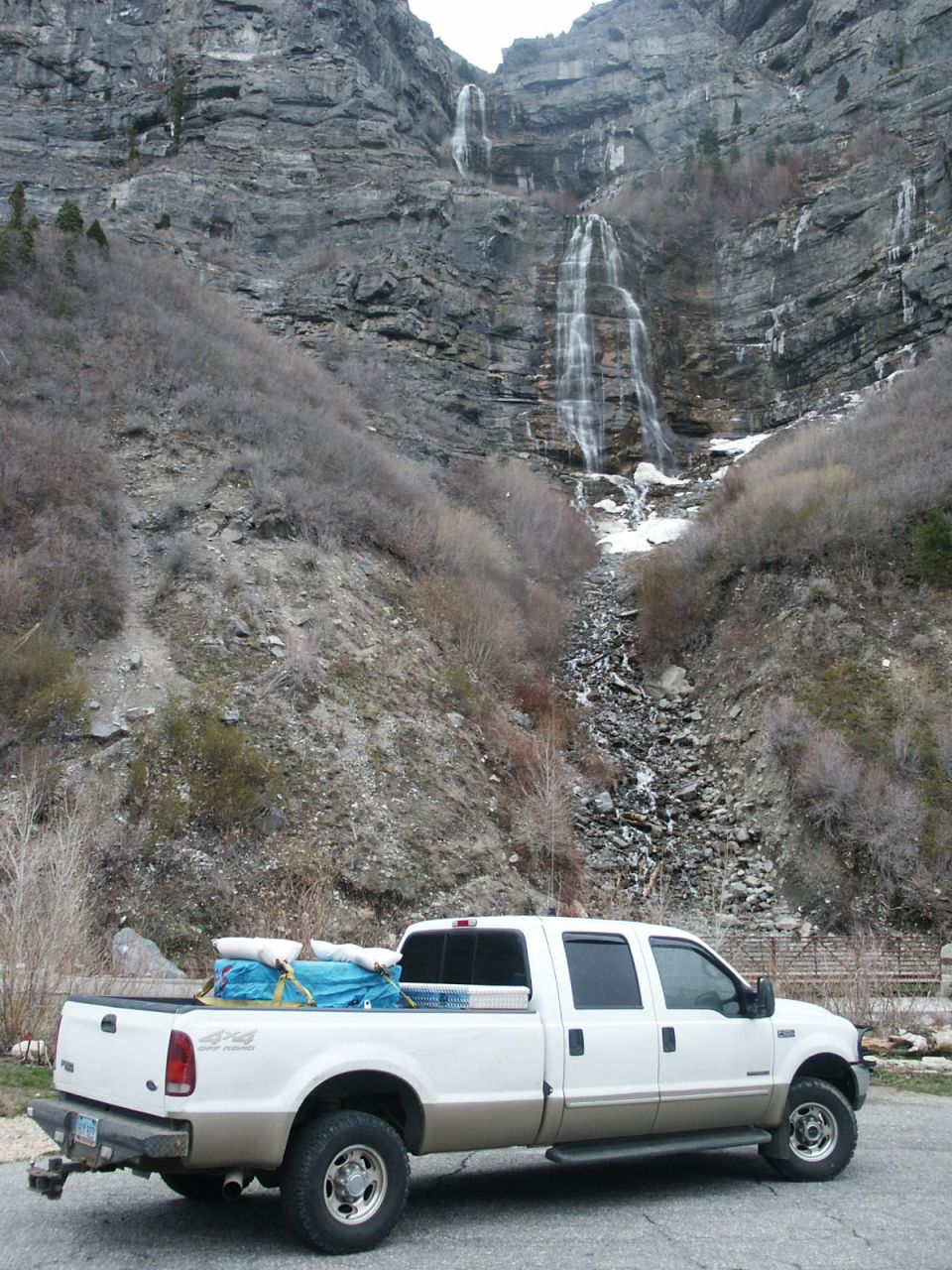 White and tan Ford F-250 pickup truck parked with a waterfall in the background