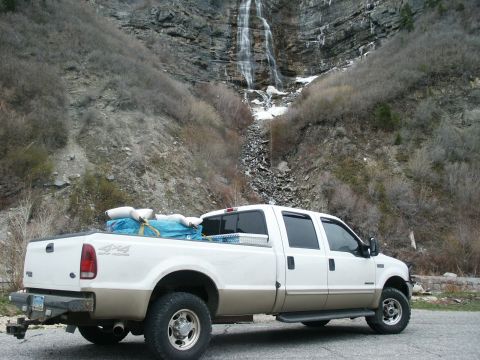 2000 Ford F-250 - A white and tan Ford F-250 pickup truck is parked on a road with a waterfall cascading down a rocky cliff face.