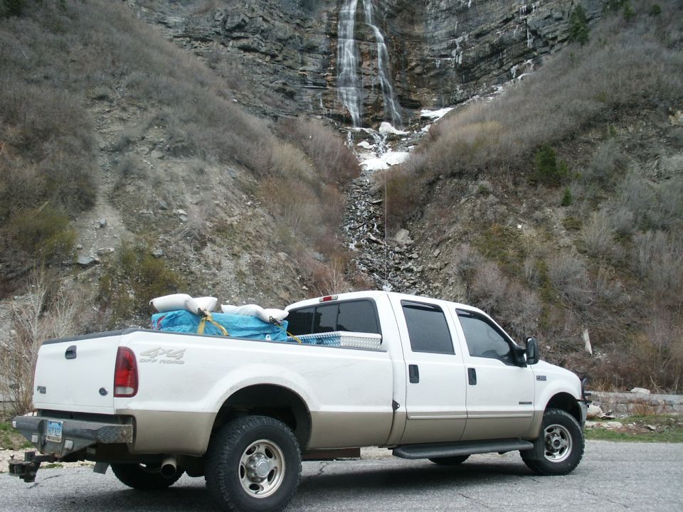 White and tan Ford F-250 pickup truck parked with a waterfall in the background