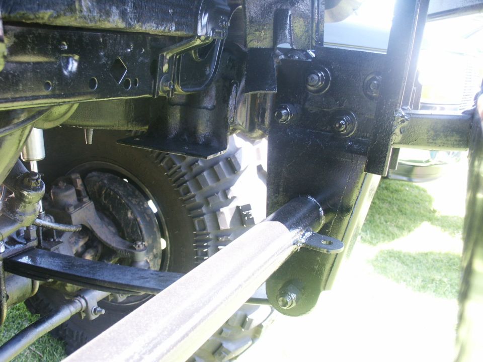 Close-up of black painted truck frame, leaf spring, shock absorber, and tire. Supermotors.net logo in lower right