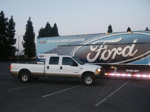 2000 Ford F-250 - A white and tan 2000 Ford F-250 Super Duty truck is parked beside a large Ford merchandise trailer.