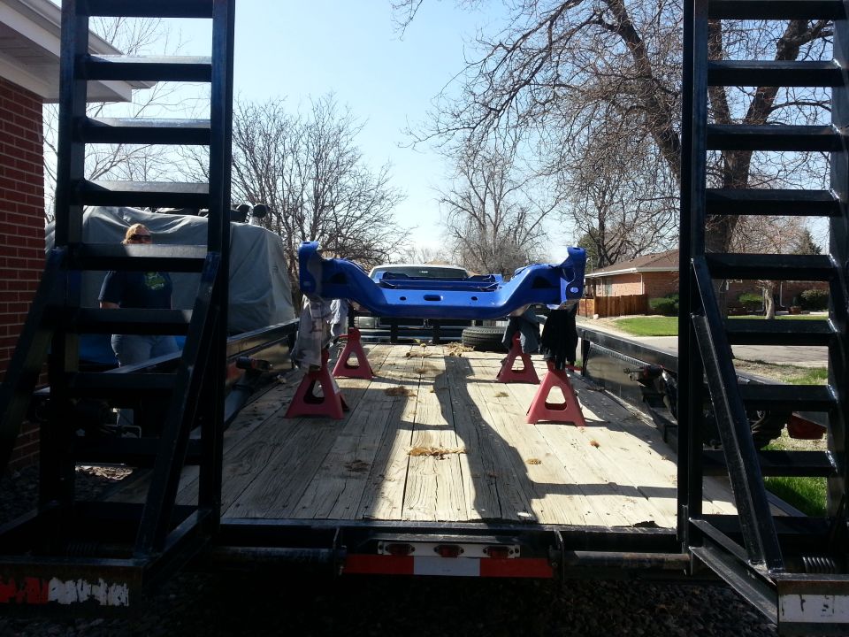 Blue painted vehicle frame on red jack stands on a trailer bed