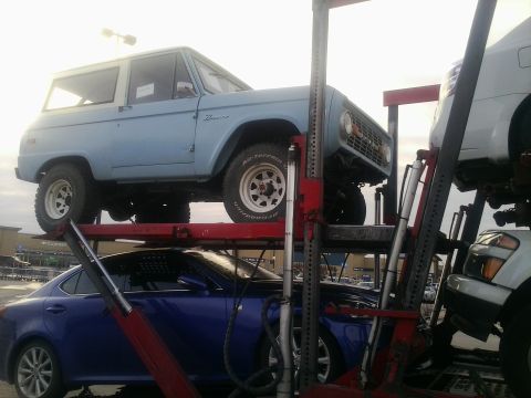 2000 Ford F-250 - A light blue Ford Bronco is seen on a car carrier, with a blue sedan below it.