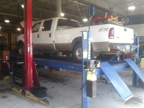 2000 Ford F-250 - A white Ford F-250 pickup truck is raised on a hydraulic lift inside a service bay.