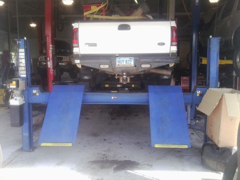 2000 Ford F-250 - A white 2000 Ford F-250 pickup truck is raised on a hydraulic lift in a repair shop.