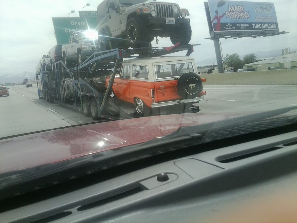 Orange Ford Bronco with spare tire on rear, on car carrier