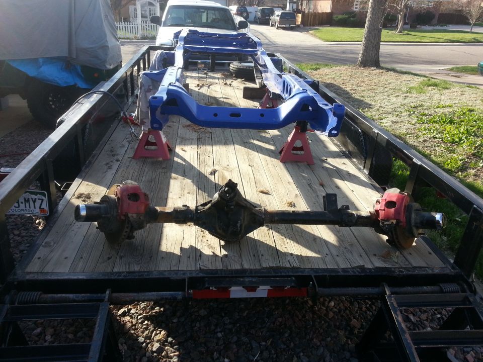 Blue vehicle frame and front and rear axles loaded on a wooden trailer