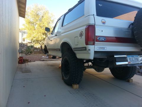 1991 Ford Bronco - Rear view of a white 1991 Ford Bronco with a lifted suspension, parked on wooden blocks.