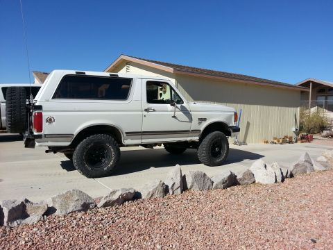 1991 Ford Bronco - This lifted 1991 Ford Bronco is parked on a rocky driveway in front of a beige house.