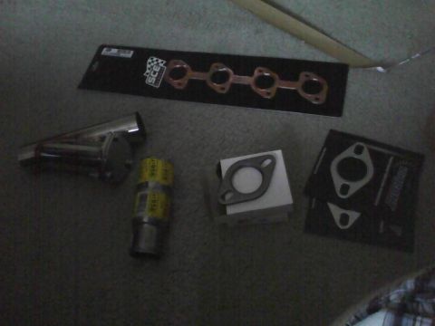 2003 Ford Crown Victoria - Several exhaust manifold gaskets and a muffler are laid out on a carpeted floor.