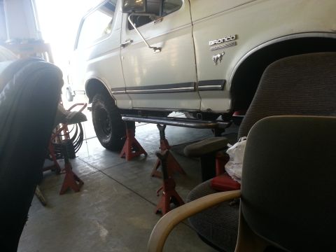 1991 Ford Bronco - A white 1991 Ford Bronco is shown from the side, elevated on jack stands in a garage.