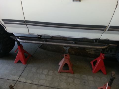 1991 Ford Bronco - Custom side steps are installed on a white SUV, which is supported by red jack stands.