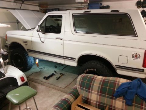 1991 Ford Bronco - A white 1991 Ford Bronco is parked in a garage with its hood open, showing some mechanical work in progress.