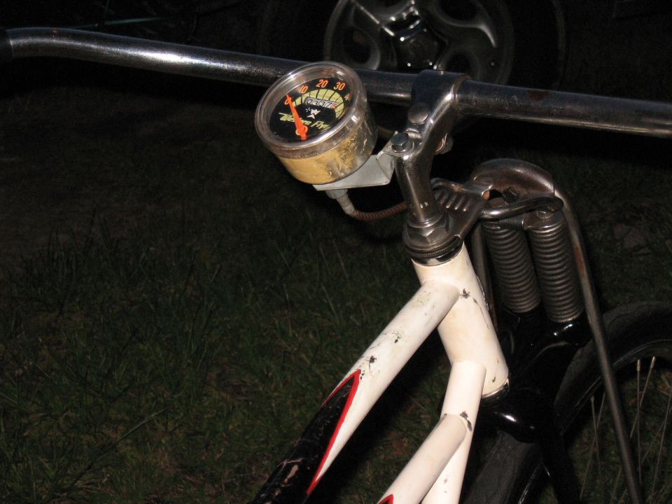 Bicycle handlebar with a speedometer gauge, chrome handlebars, and white frame with red and black accents