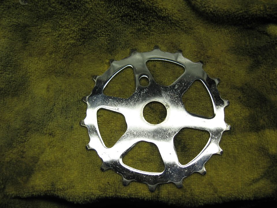 Chrome bicycle chainring with 5 large cutouts and 18 teeth, resting on a green cloth