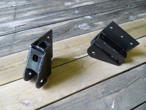 1992 Ford Bronco - Two black metal suspension components are displayed on a weathered wooden surface.