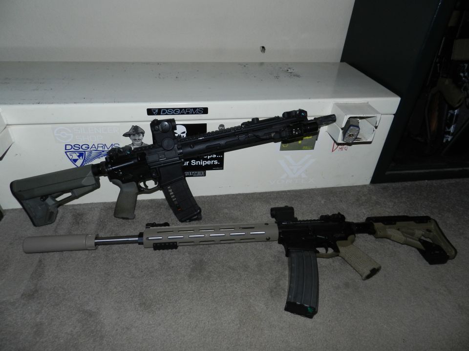 Two rifles are on a carpet in front of a white safe with stickers