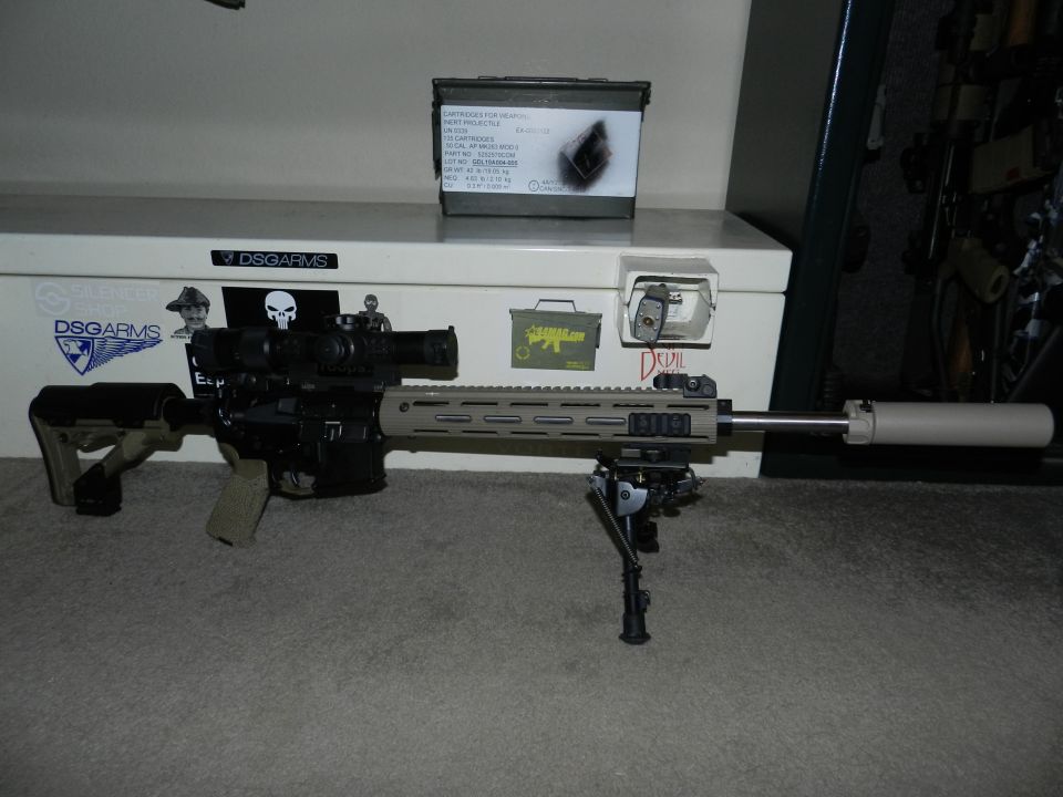Assault rifle with scope, bipod, and suppressor. Ammo can and stickers on a chest behind it