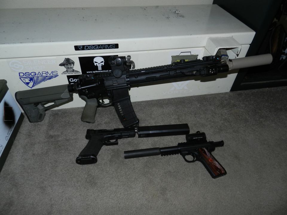 AR-15 style rifle, pistol, and another handgun with suppressors on a carpet