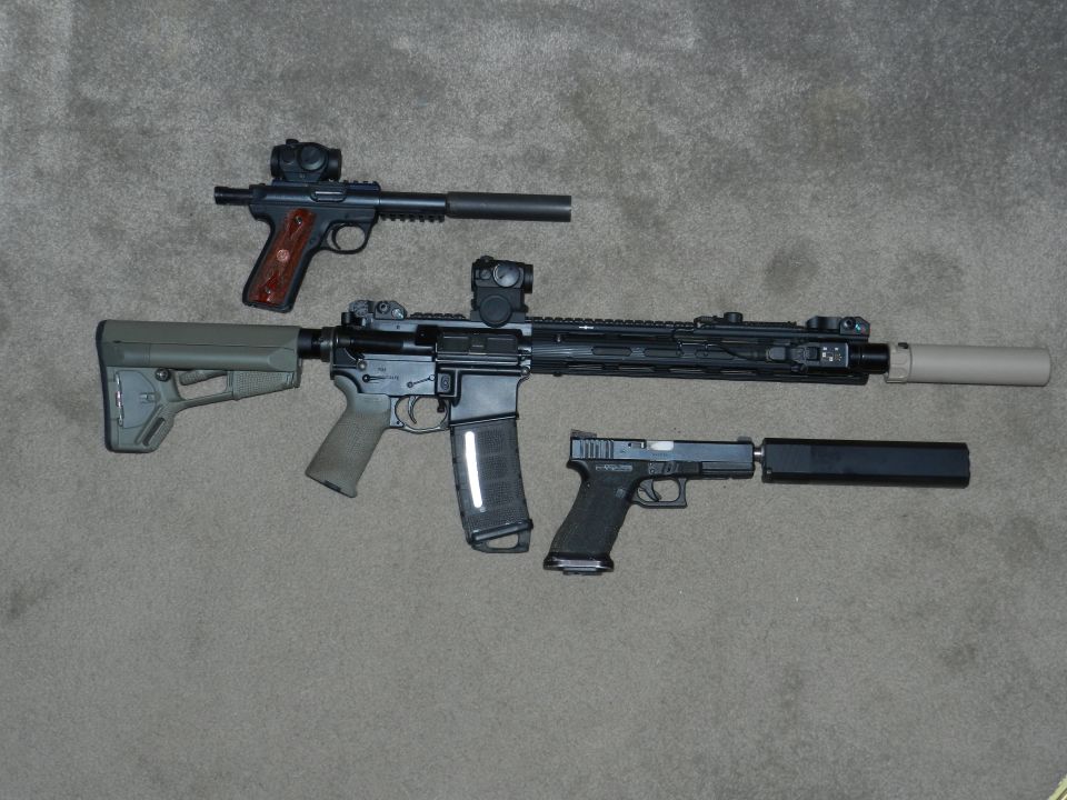 Three firearms with suppressors on a carpeted surface