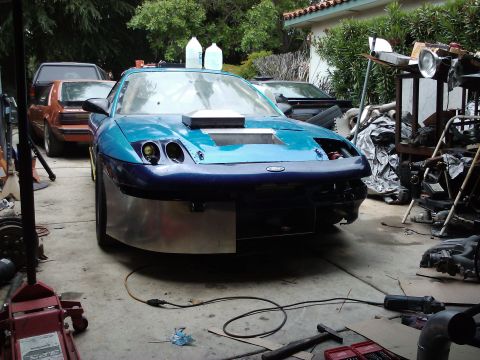 1995 Ford Probe - A modified sports car sits in a driveway surrounded by tools and other vehicles.