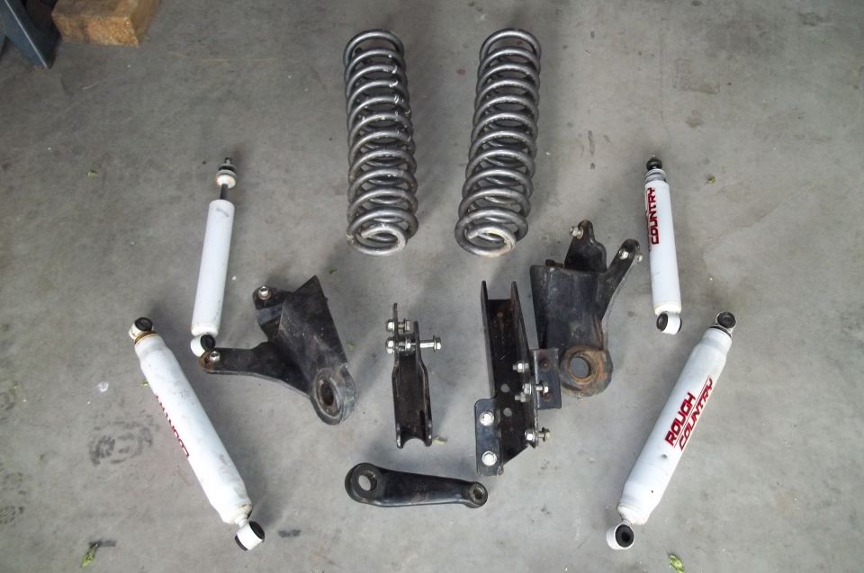 Coil springs and shock absorbers laid out on a concrete floor. Some brackets are also visible