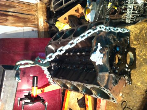 1996 Ford Bronco - Engine block is mounted on an engine stand and held by a chain, ready for work.